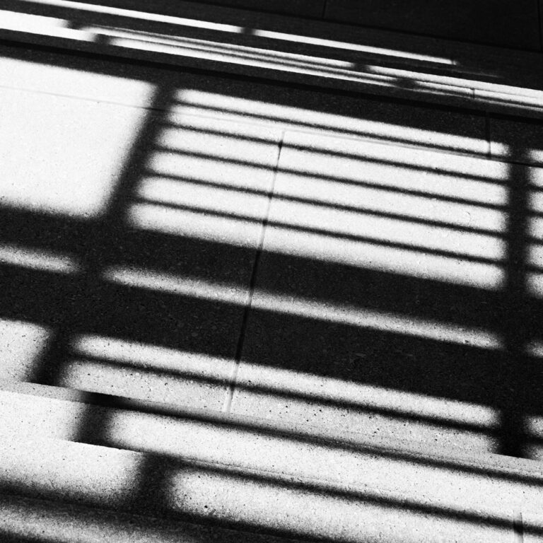 Abstract photography in black and white: the shadow of a railing falling in diagonal stripes across a wall