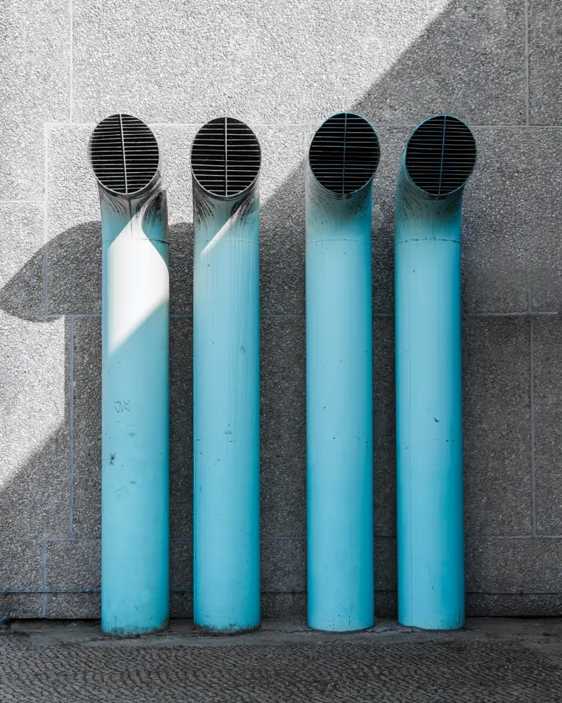 Four turquoise ventilation pipes on a grey concrete wall, Berlin
